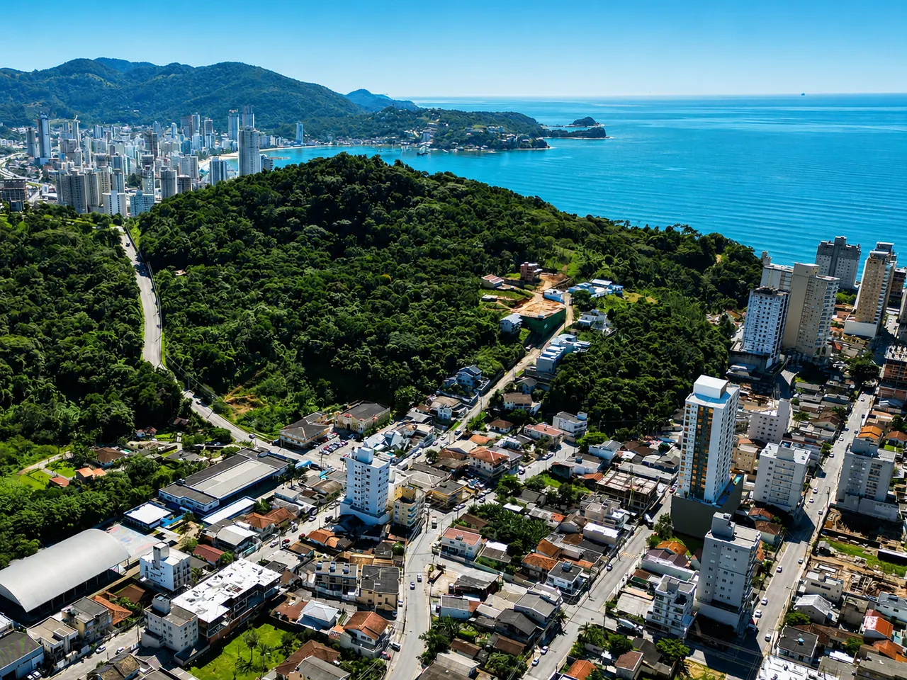 Vista aérea do bairro Morretes, com o morro coberto de mata e o mar ao fundo